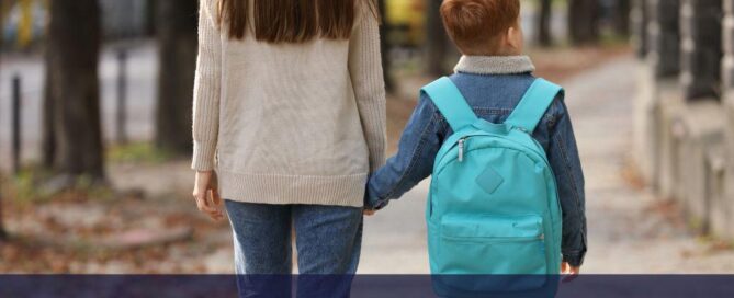 mom and son with a blue backpack walking to school on a path